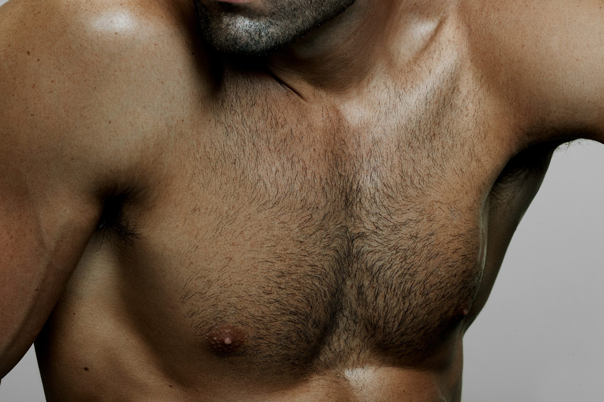 The broad plain of the chest, grain of skin and hair mapped by a single key light.