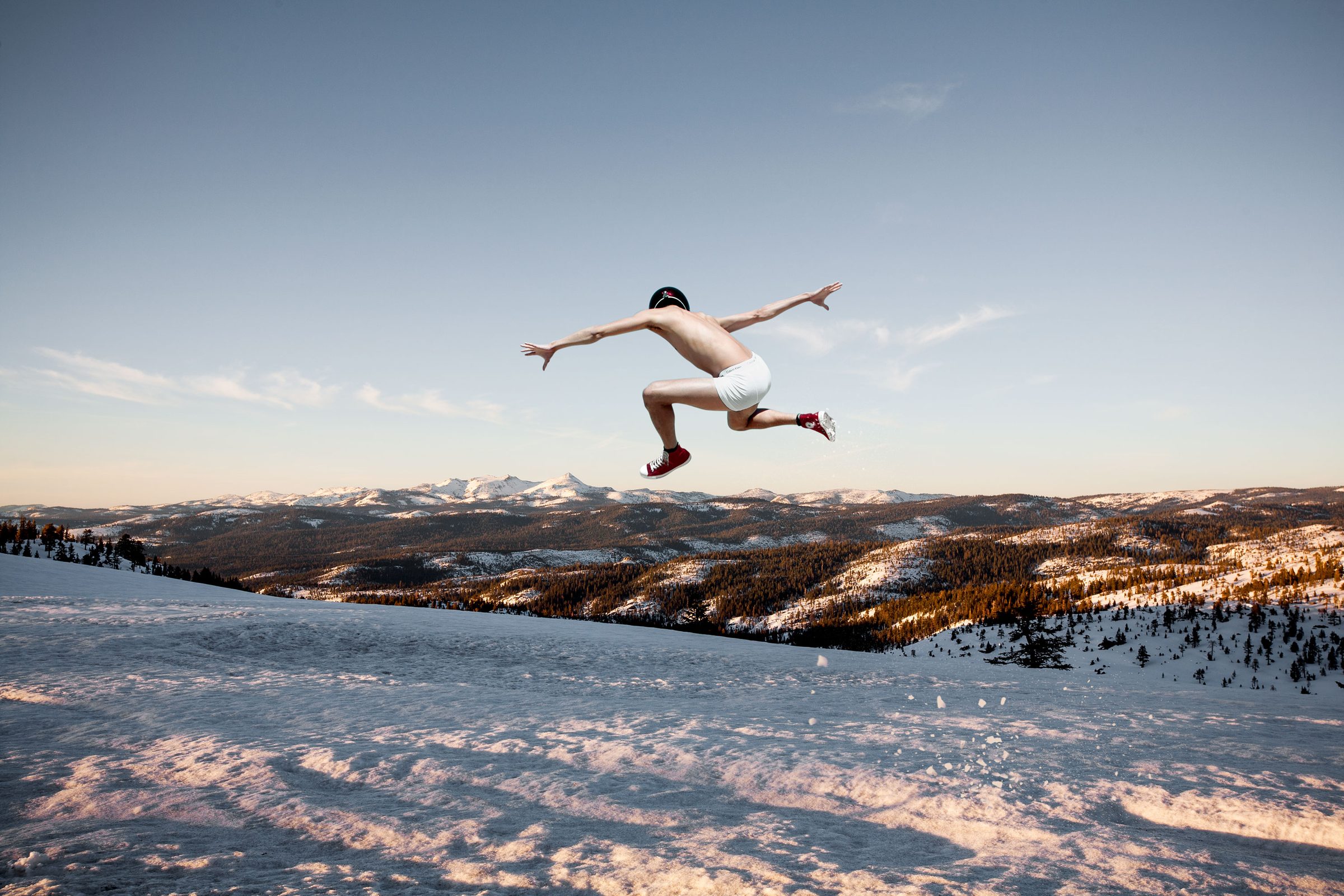 A leap over the snowfield — red sneakers, bare limbs, and a mountain horizon.