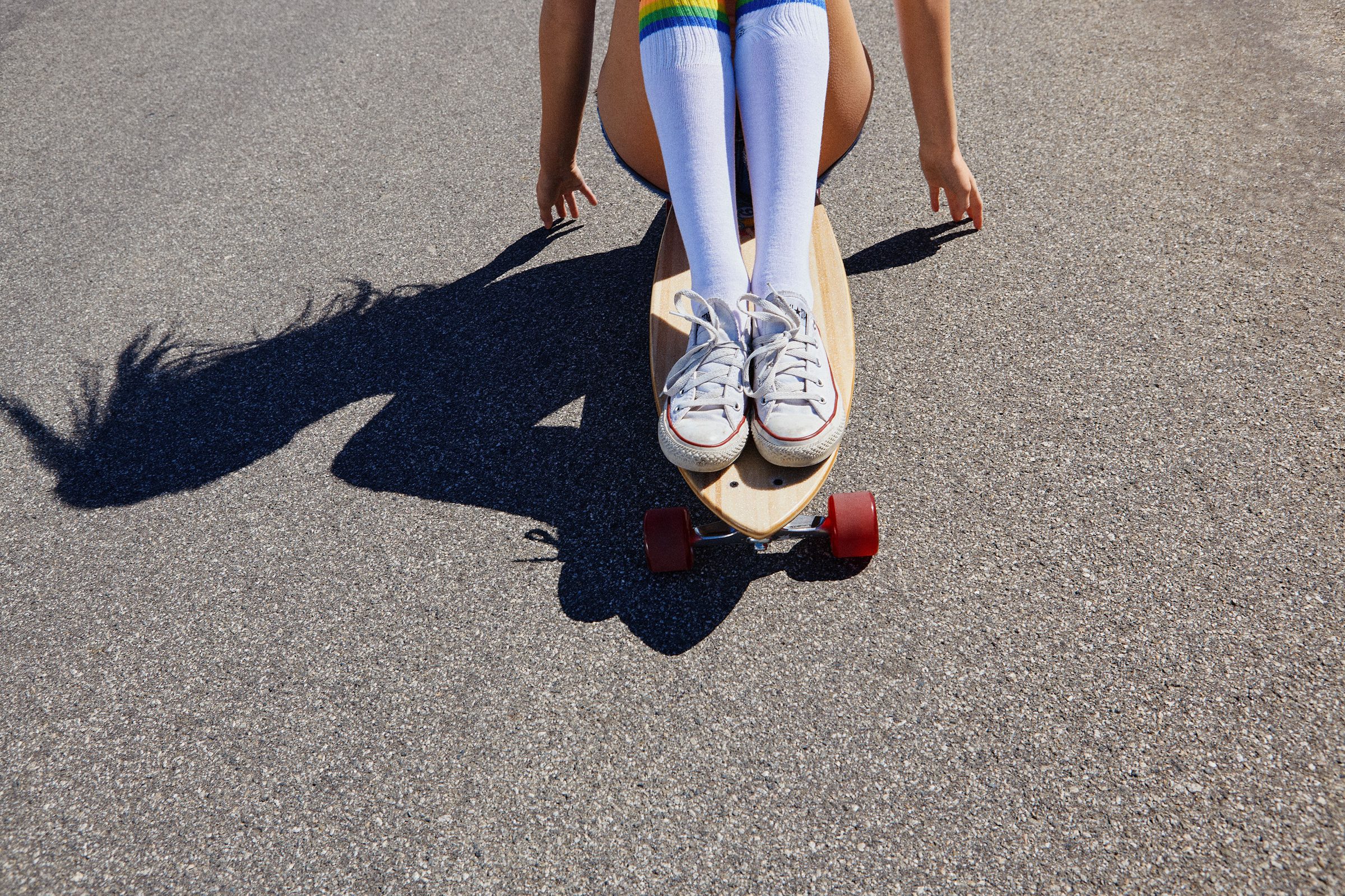 Rainbow-striped knee socks and white sneakers balanced on a longboard.