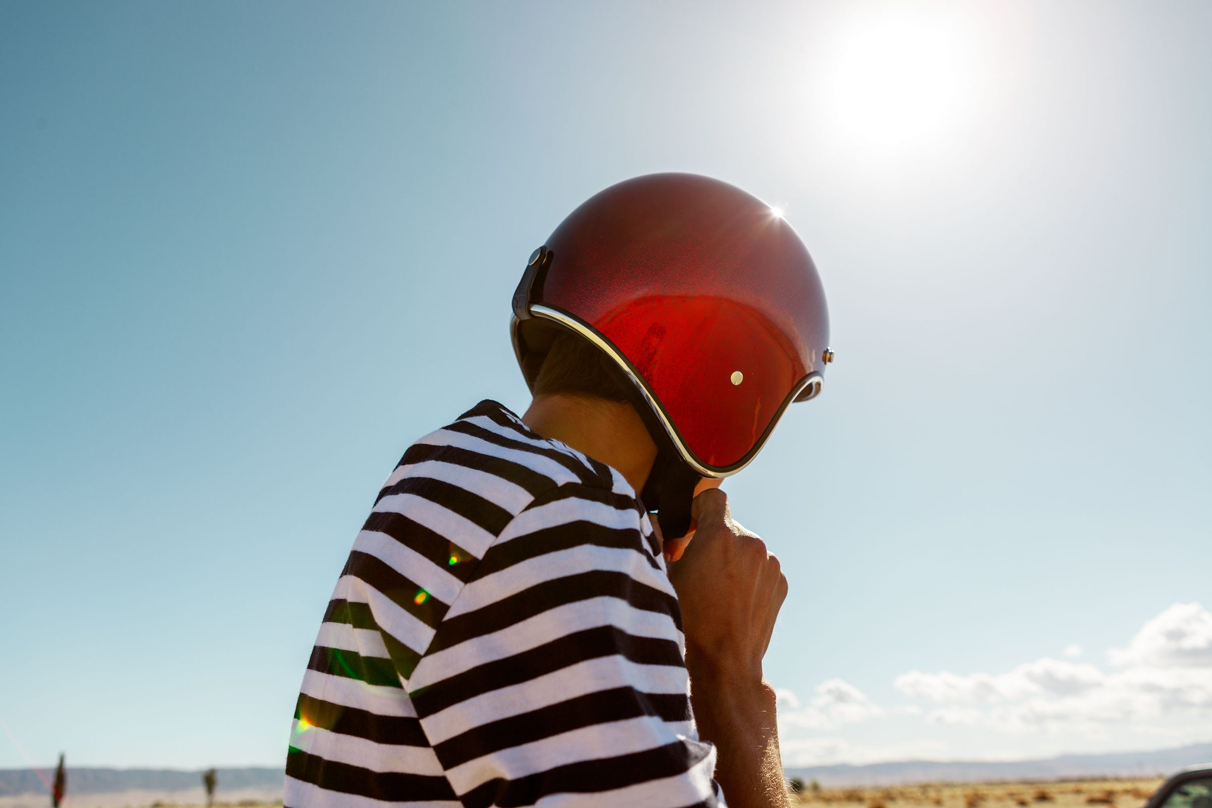 The rider cinches his red helmet against a hard blue sky.