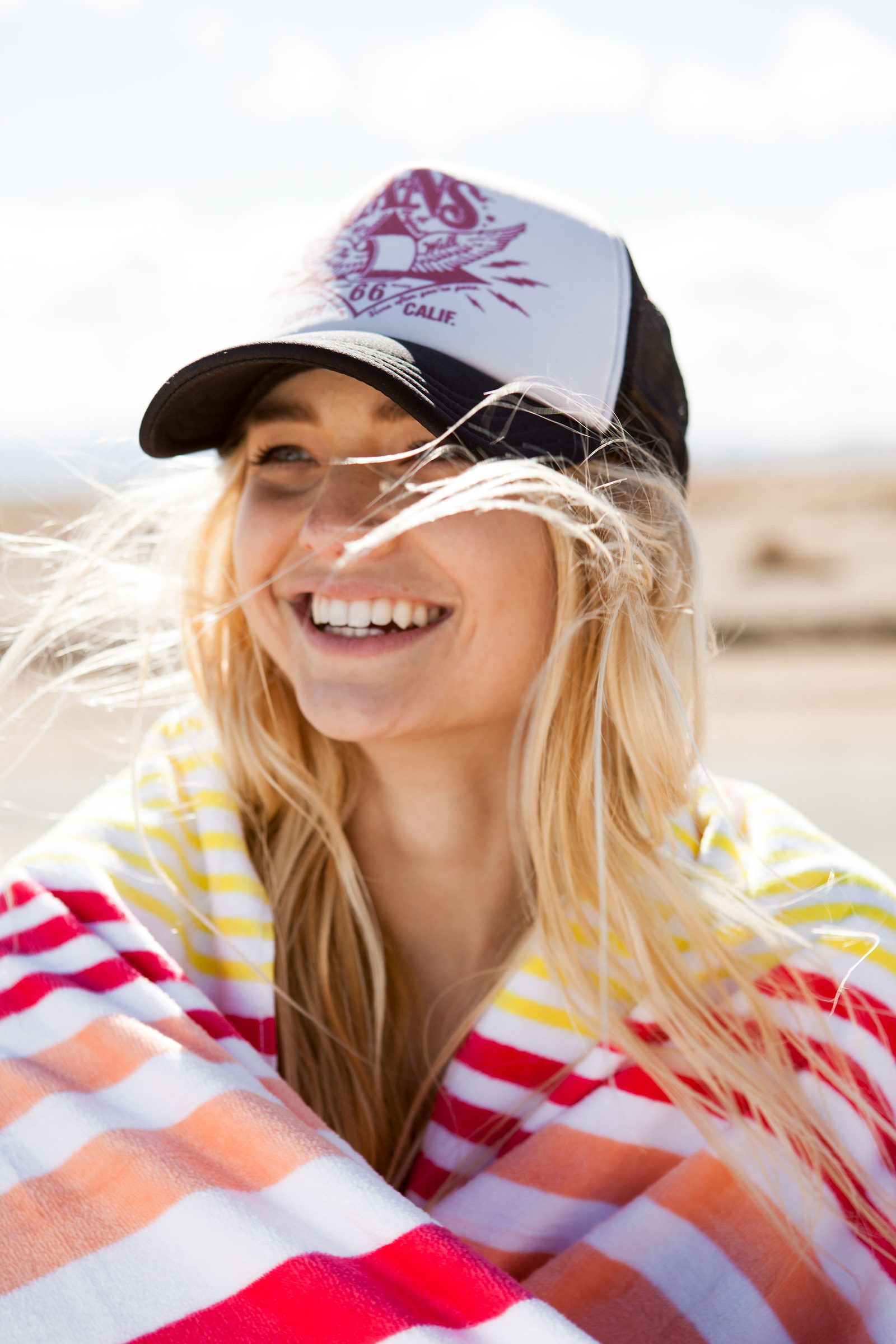 Wrapped in a striped beach towel and a trucker cap, she laughs into the wind.