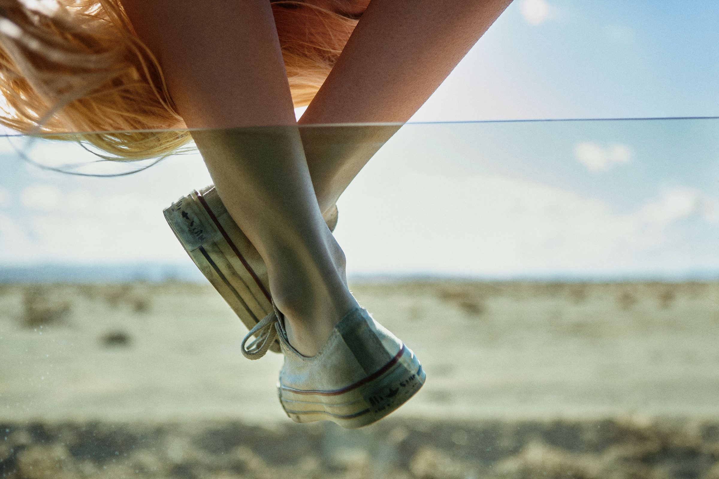 Worn sneakers ride the window glass, desert scrub sliding past beneath.