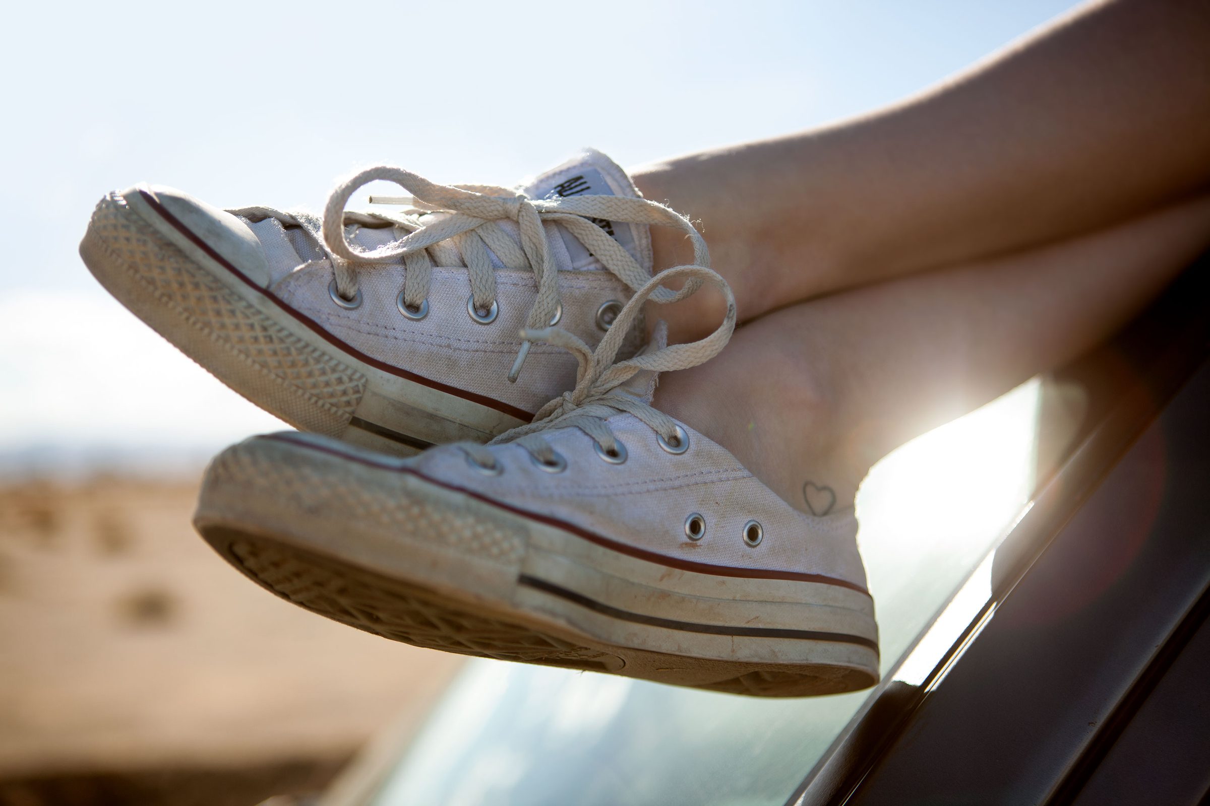 White Converse crossed at the ankle, catching the last hard light.