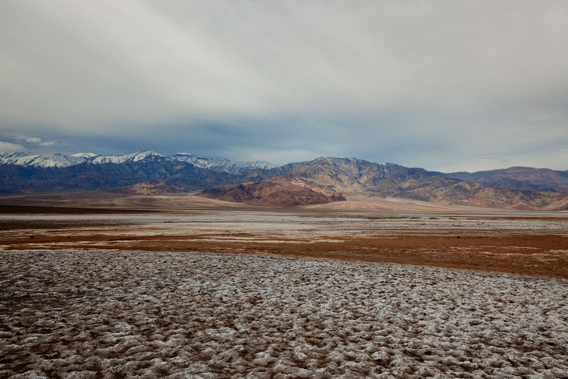 Sun-bleached salt flats cracking toward snow-capped ranges in the California desert.