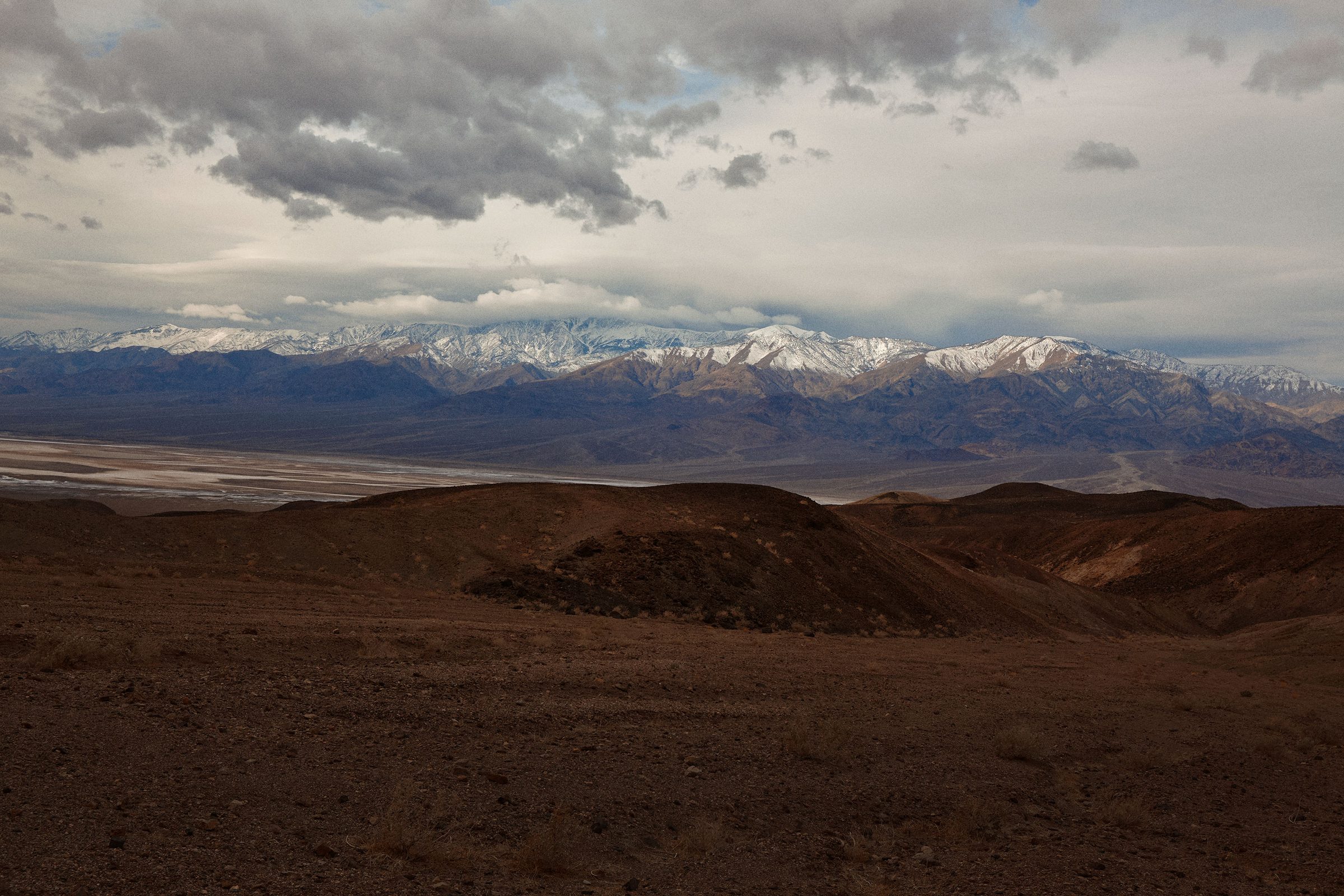 Storm clouds gather over dark volcanic hills and a distant snowline.