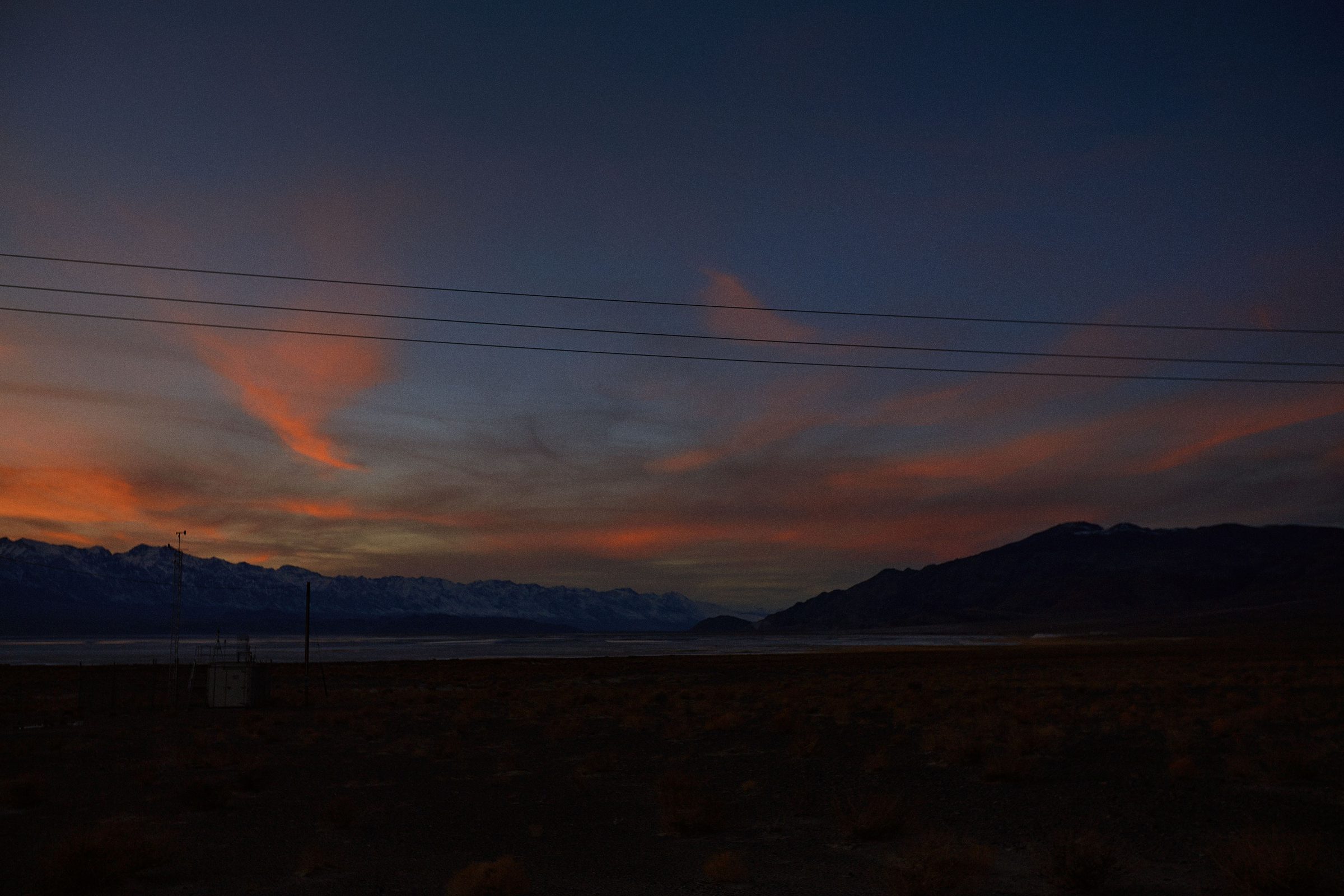 Dusk ignites the clouds above a California desert valley laced with power lines.