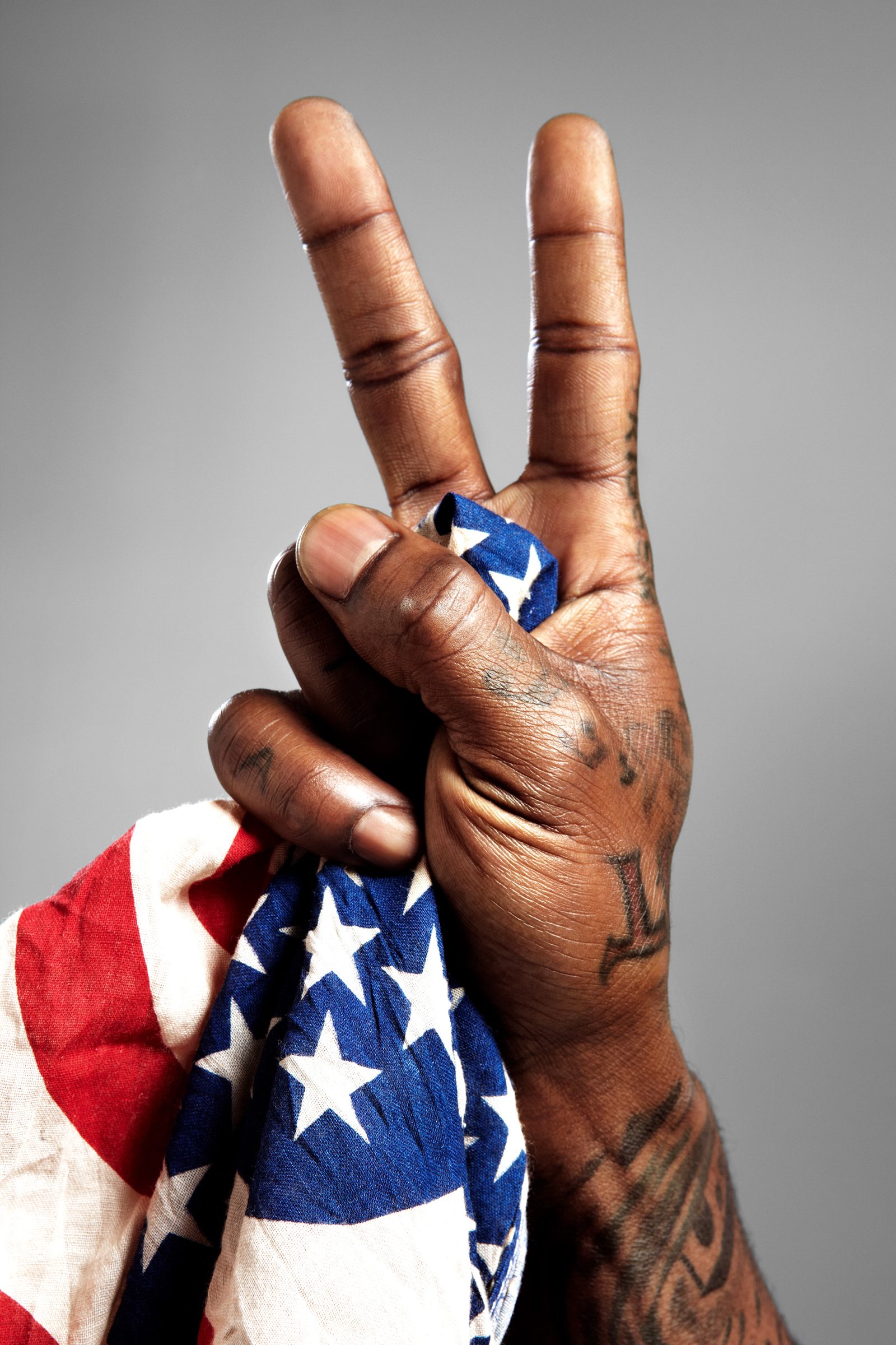 Tattooed fingers fold a peace sign into an American flag bandana.