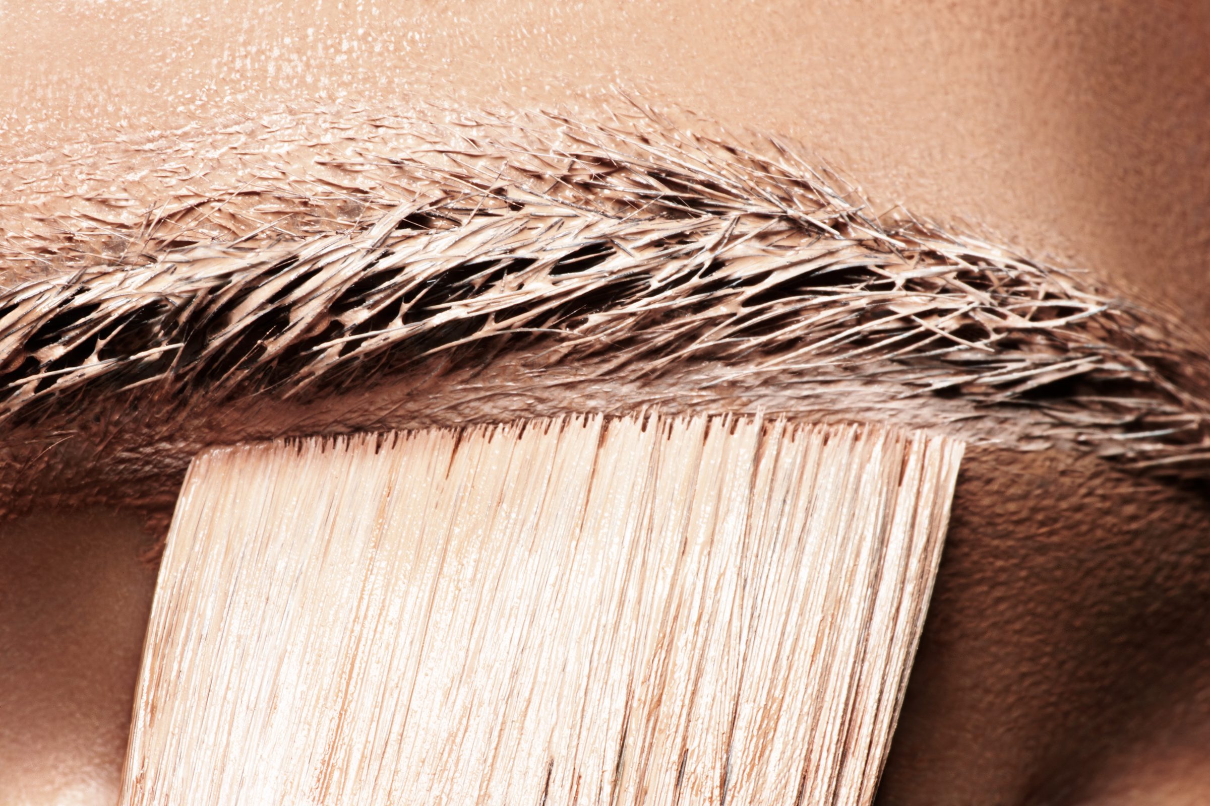 The brush sweeps skin-tone pigment through the arch of a brow, hair by hair.