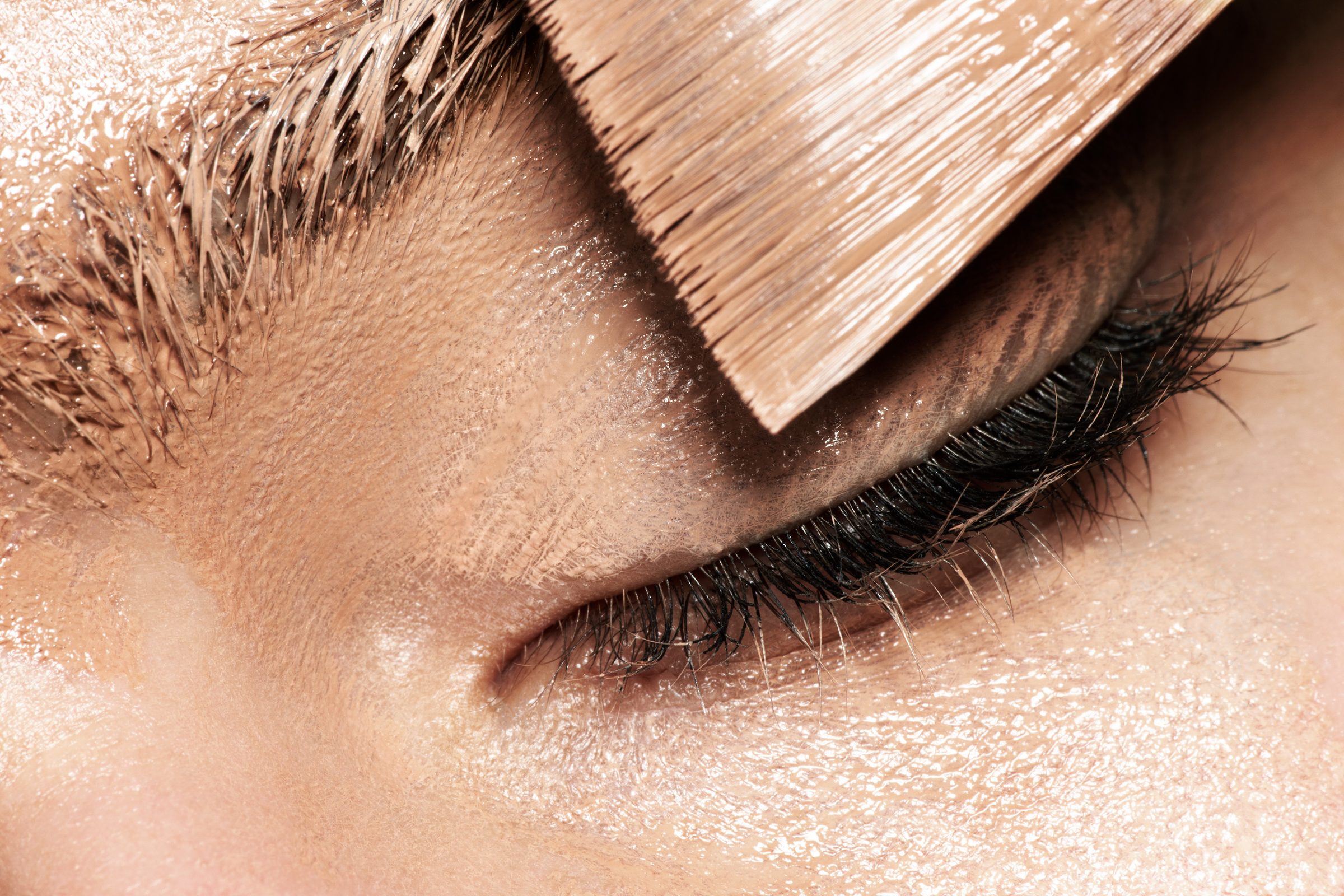 Paint-stiffened bristles descend over a closed eye, lashes untouched black.