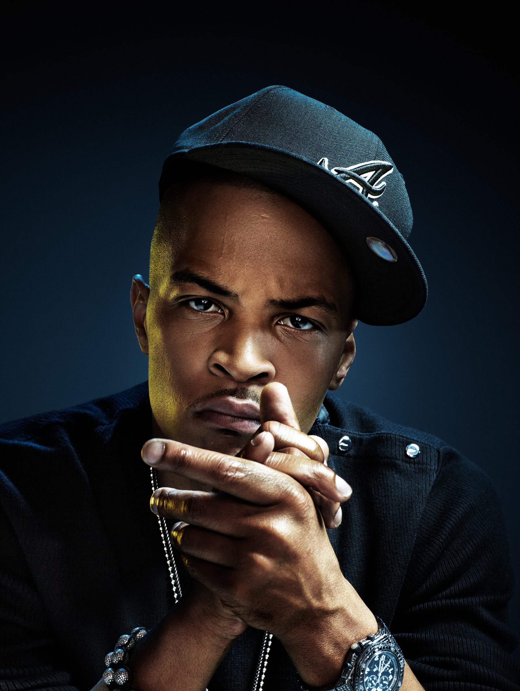 T.I. in an Atlanta Braves cap, hands clasped before his face, against a deep blue backdrop.