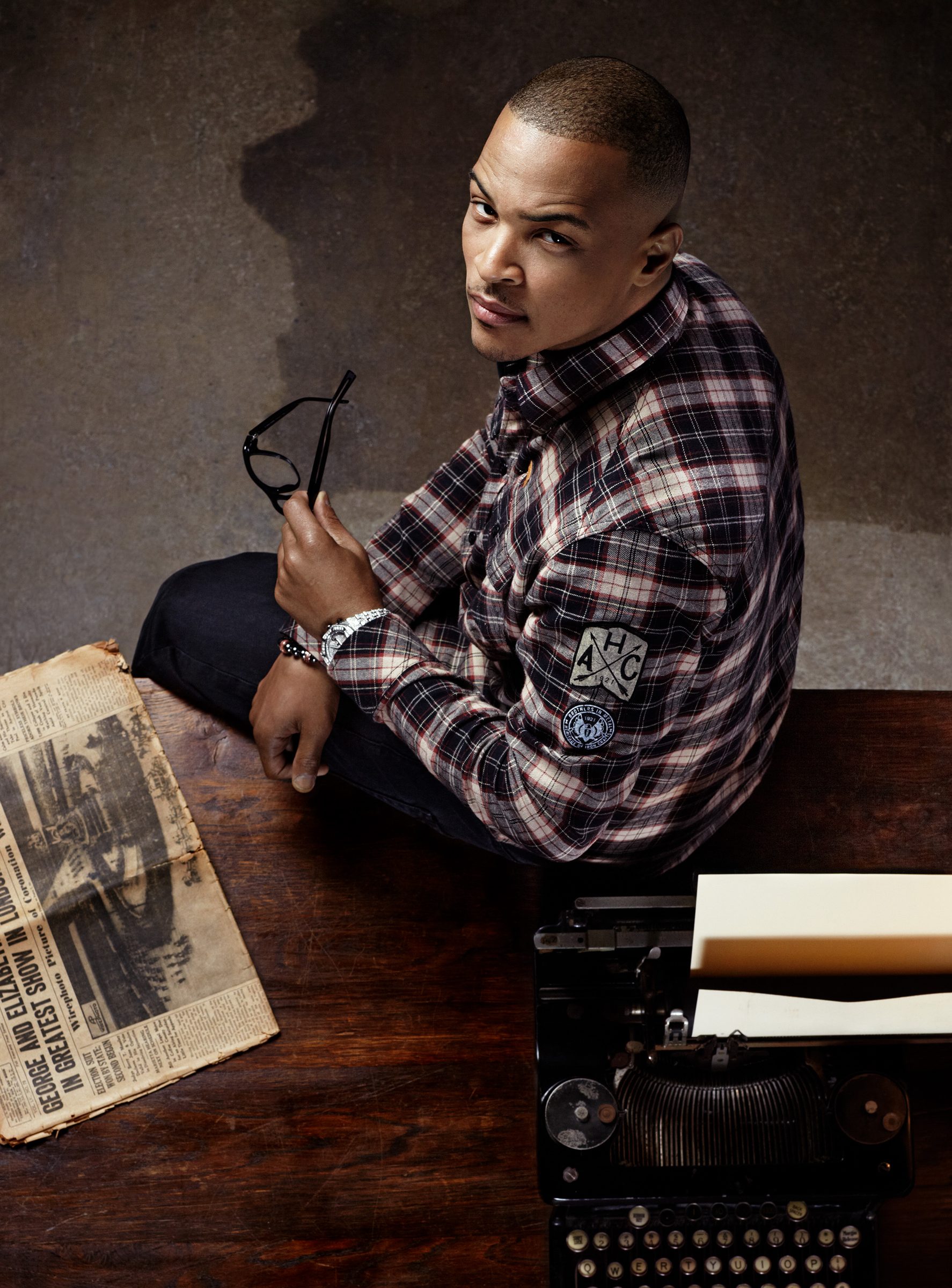 T.I. glances back from the writing desk, glasses in hand, typewriter loaded with a fresh page.