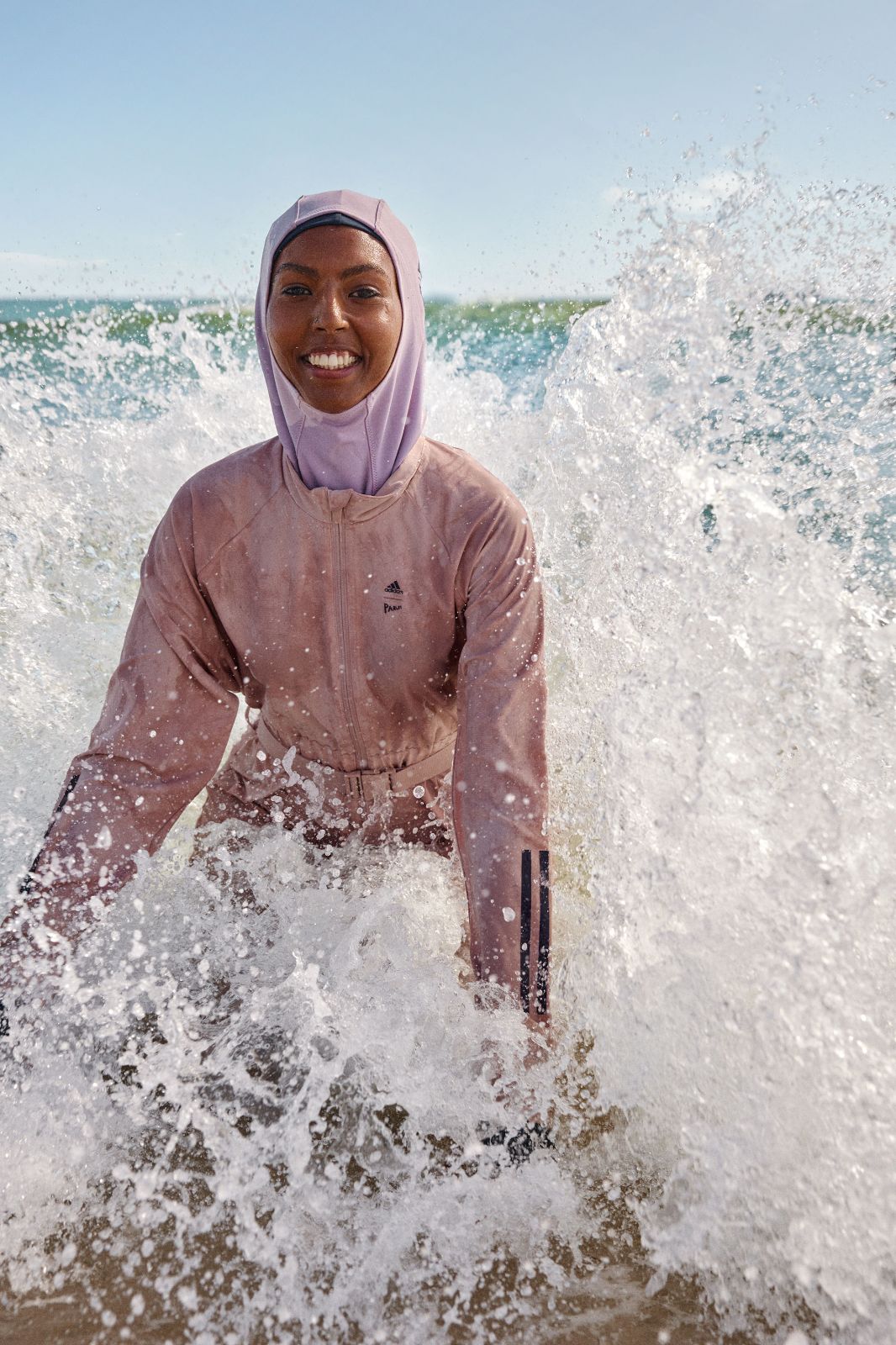 Woman in stylish pink burkini splashing beautifully in crashing ocean waves