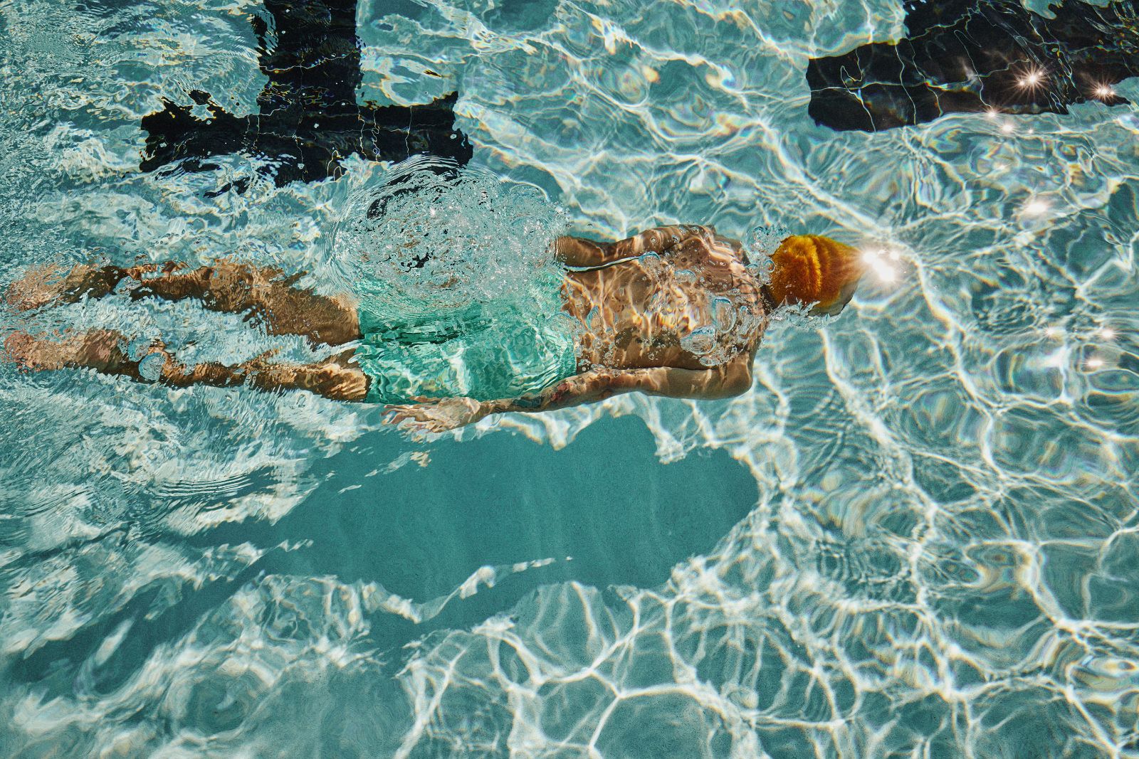Swimmer gliding weightlessly through sunlit turquoise pool water causing bright optical distortions