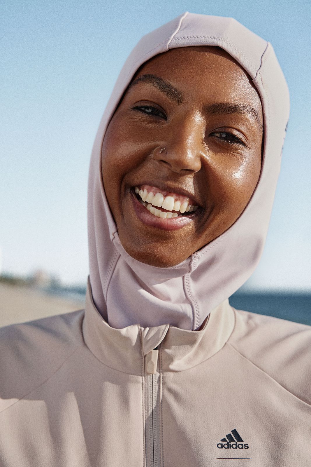 Smiling woman wearing a stylish pale pink sports hijab at the beach