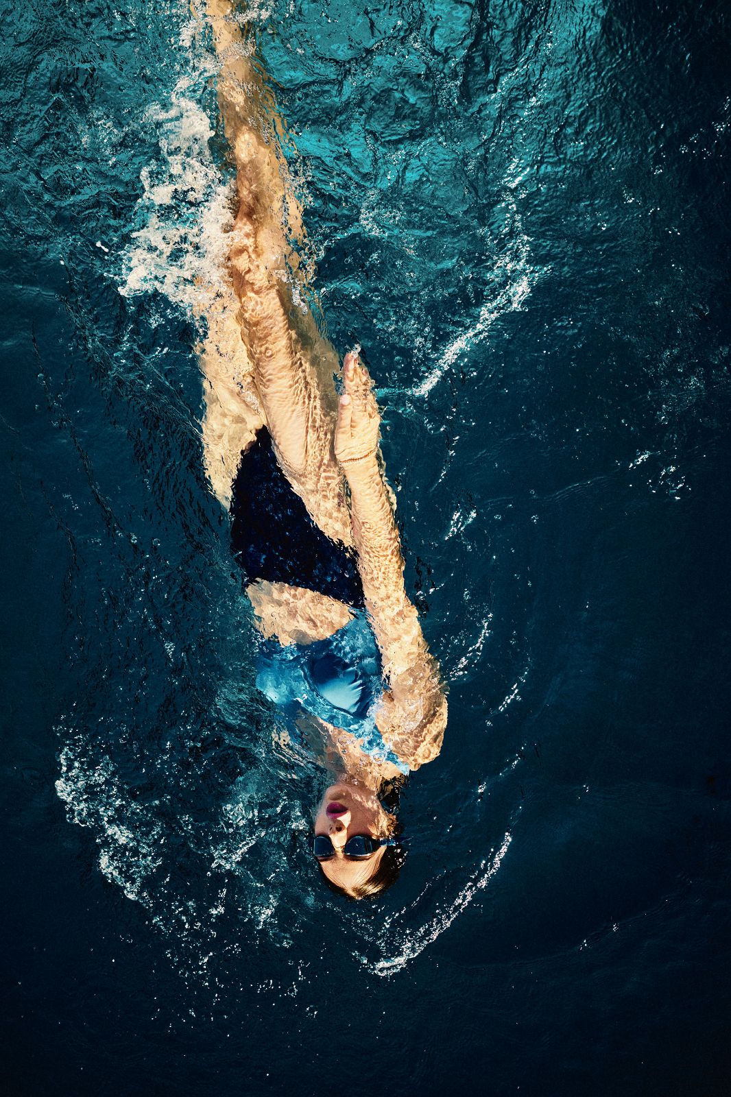 Overhead view of woman backstroking elegantly through deep blue rippling water