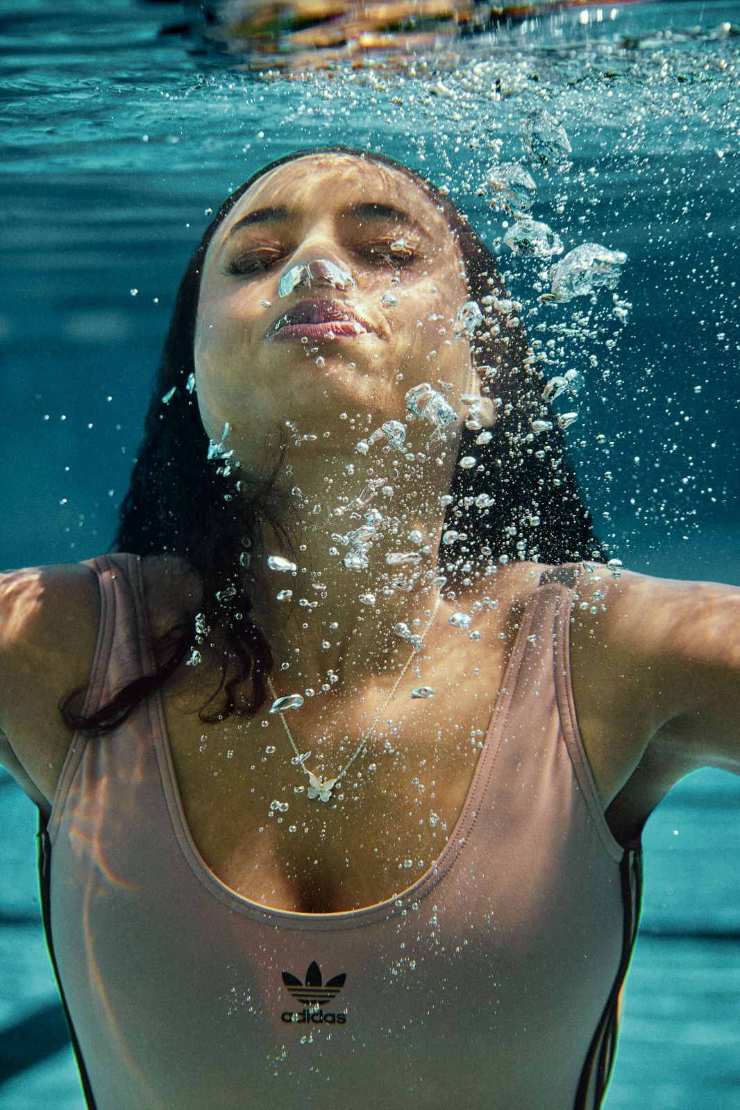 Woman exhaling silver bubbles directly below a bright turquoise pool surface