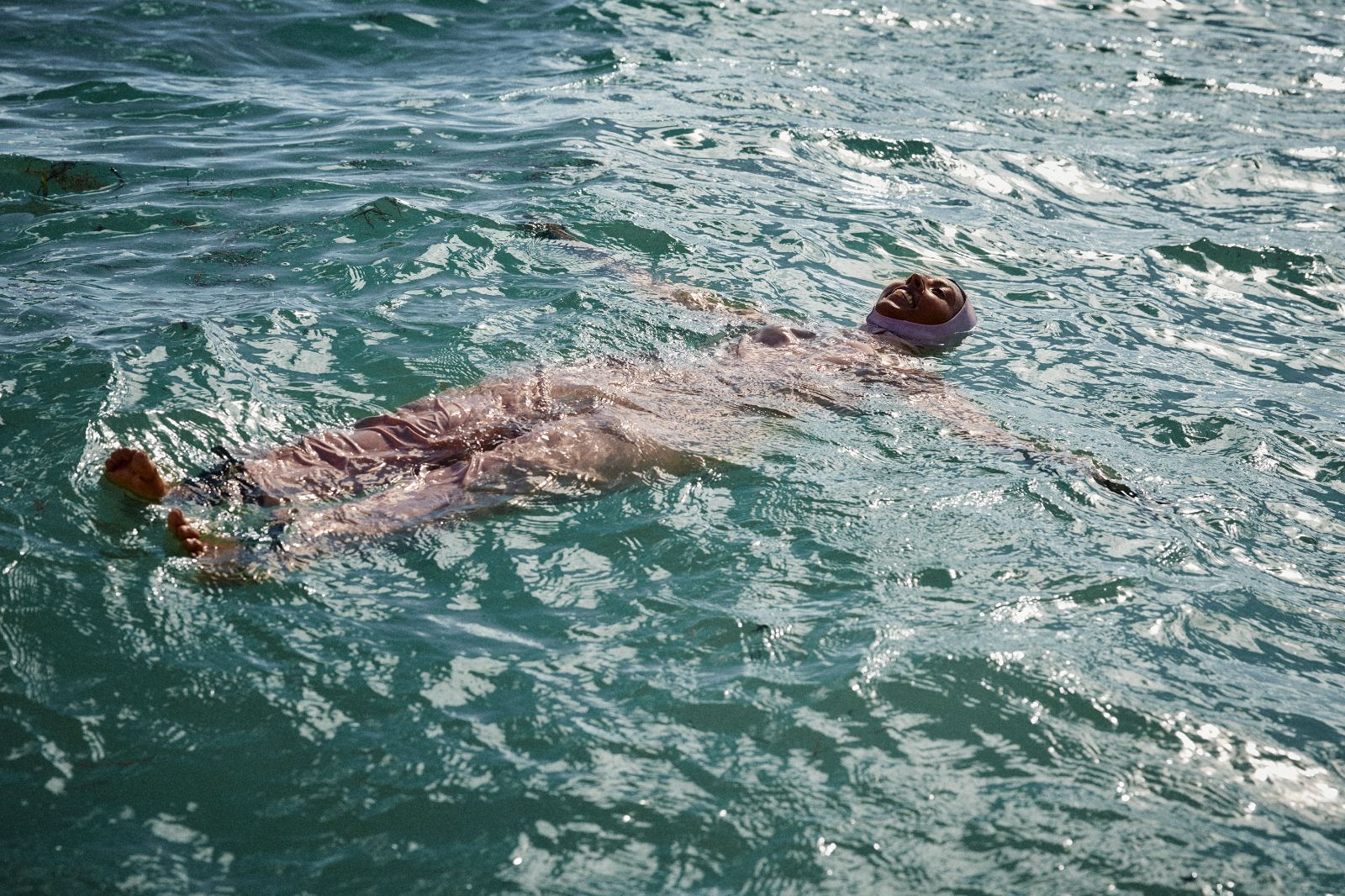 Serene woman floating in sweeping pink burkini on shimmering turquoise ocean