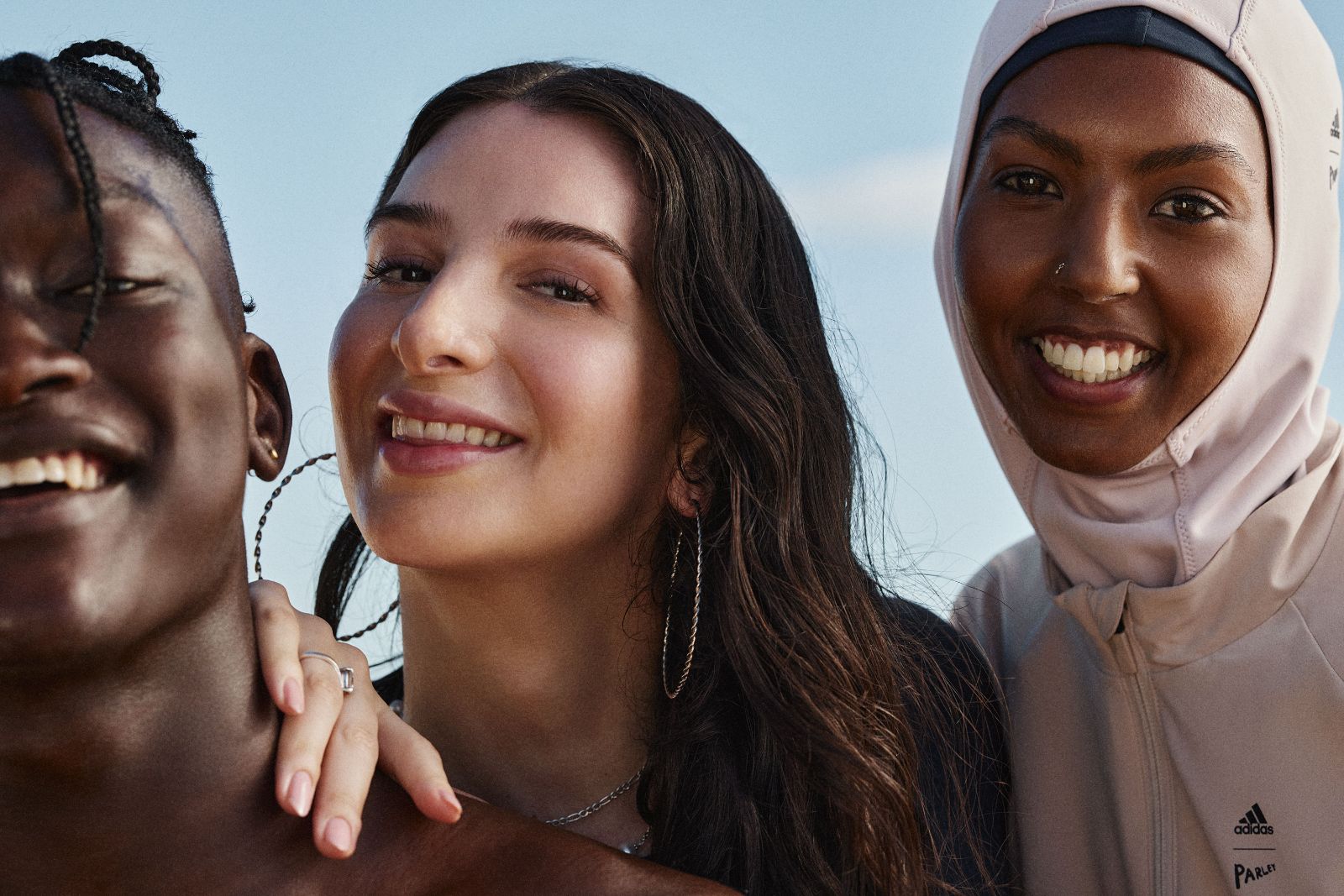 Three diverse joyful friends smiling closely together against clear summer sky