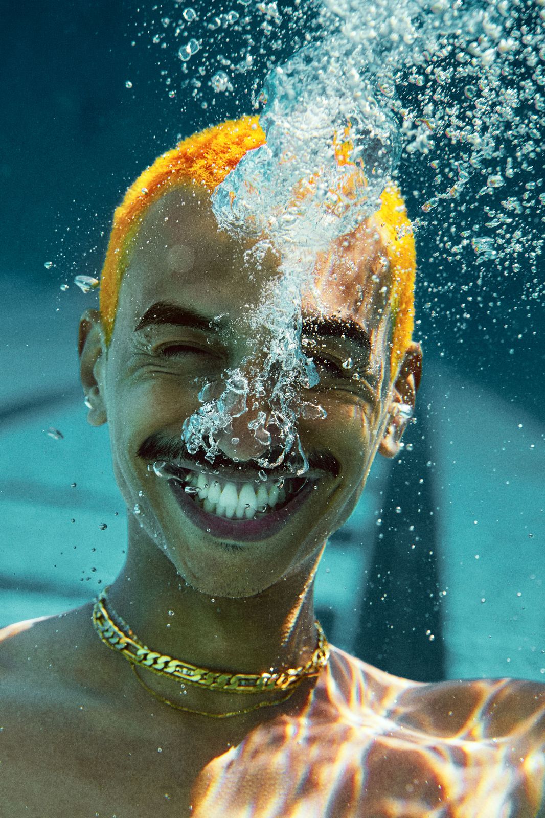 Orange haired man exhaling silver bubbles and smiling joyfully underwater