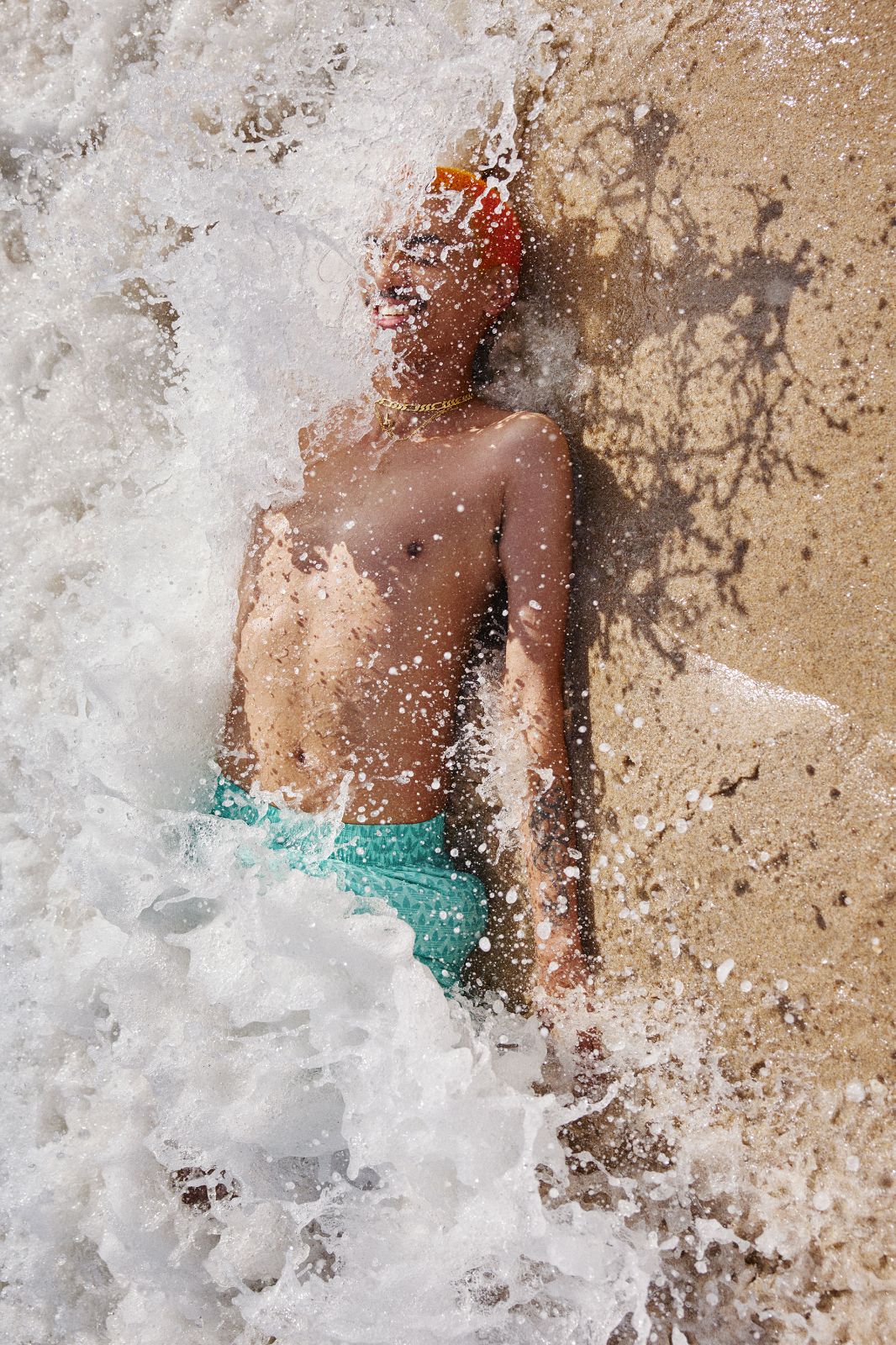Laughing young man with vibrant orange hair splashed by white ocean wave