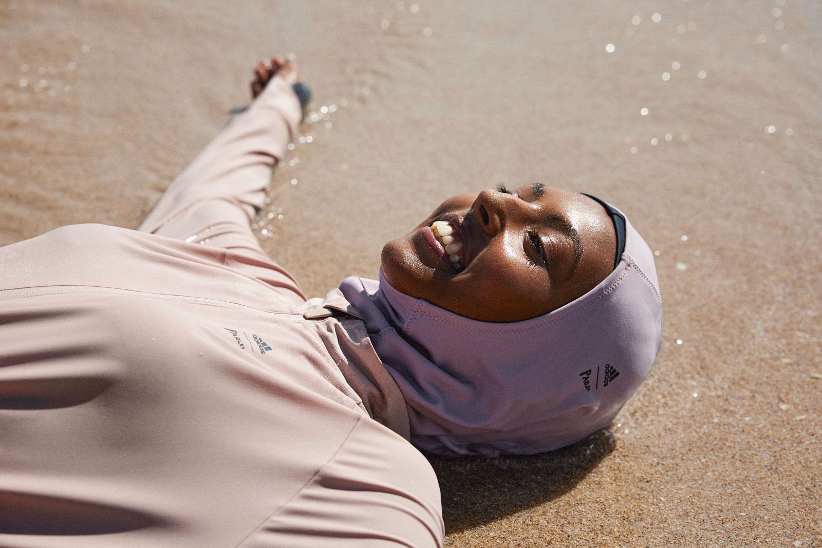 Woman in lavender hijab swimsuit lying gracefully on wet ocean sand