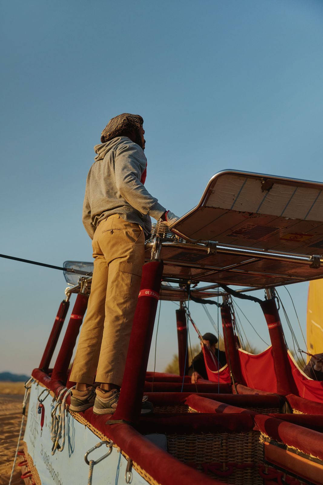 A guide standing on the edge of a hot air balloon basket at dawn.