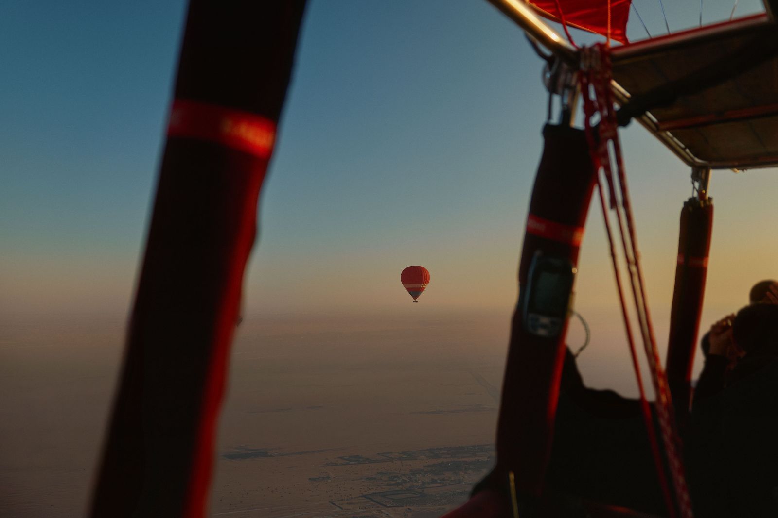 View past red structural ropes of a hot air balloon toward another in the sky.