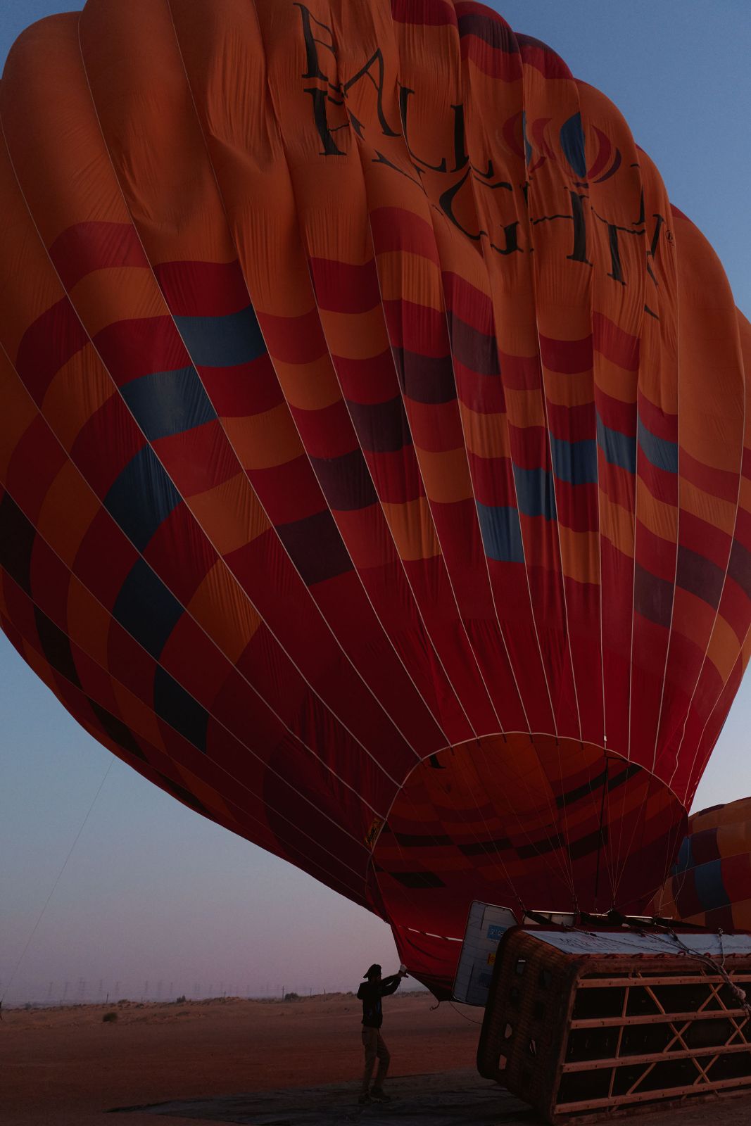 A massive brightly colored hot air balloon inflating on the sandy flatland.