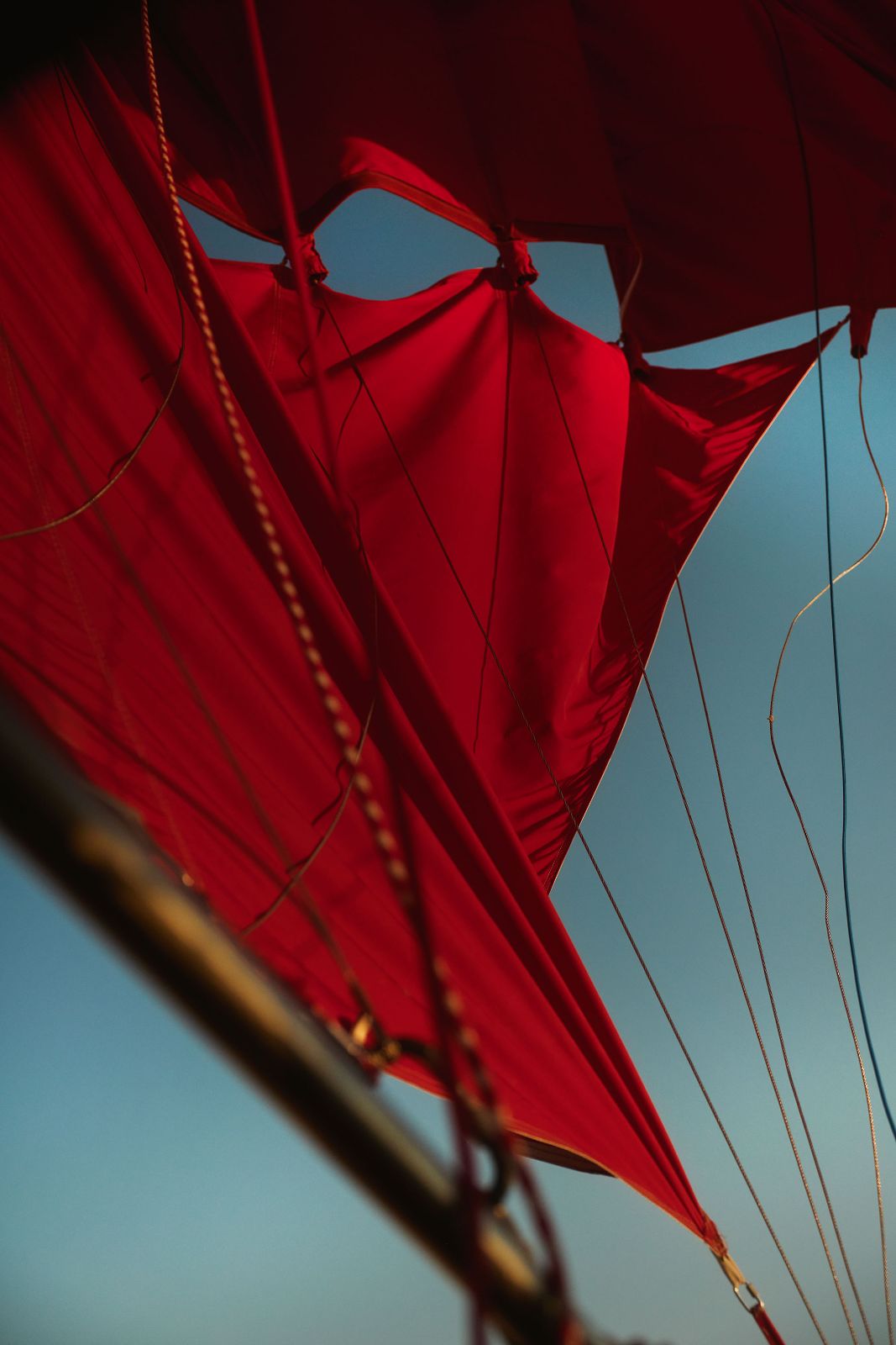 Vibrant red balloon fabric pulled taut by rigging against a deep blue sky.